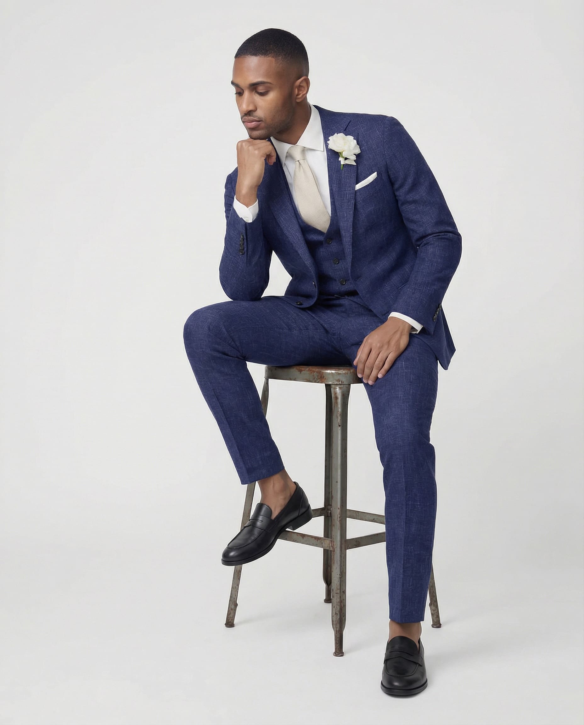 Mann im mittelblauen Anzug mit Weste auf dem Hocker sitzend