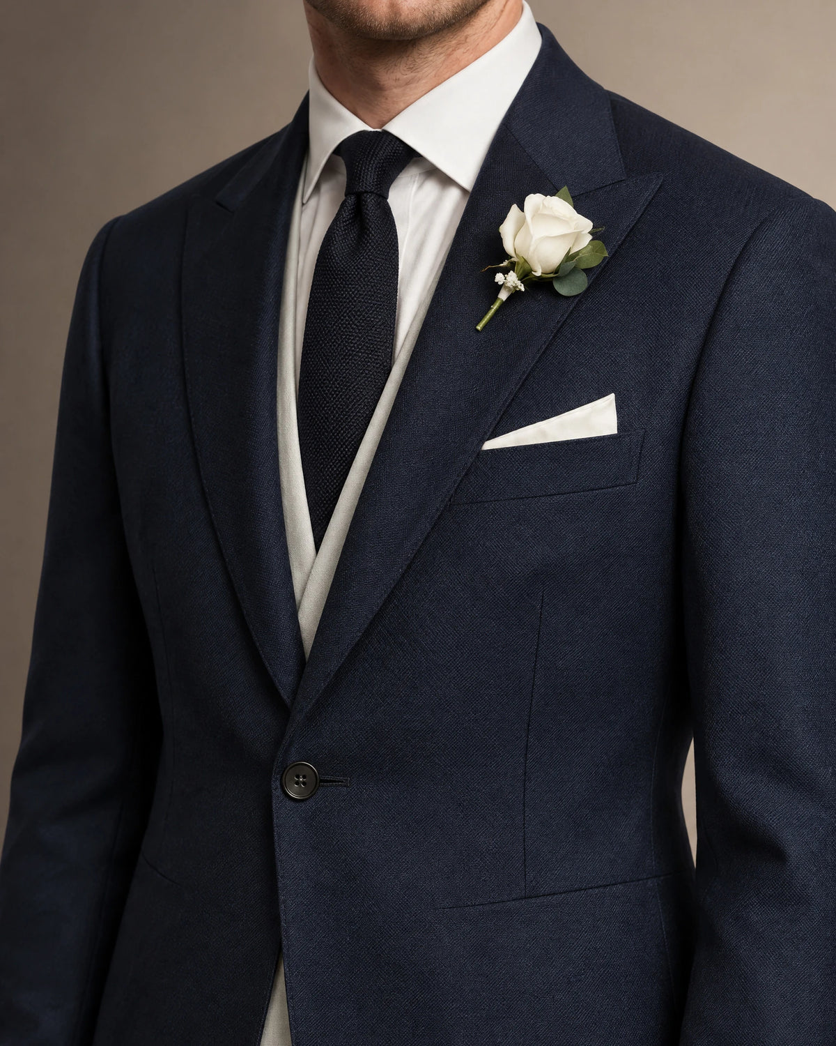 Nahaufnahme des blauen Cutaways mit steigendem Revers, weißer Ansteckrose, Einstecktuch, beiger Weste und Strickkrawatte