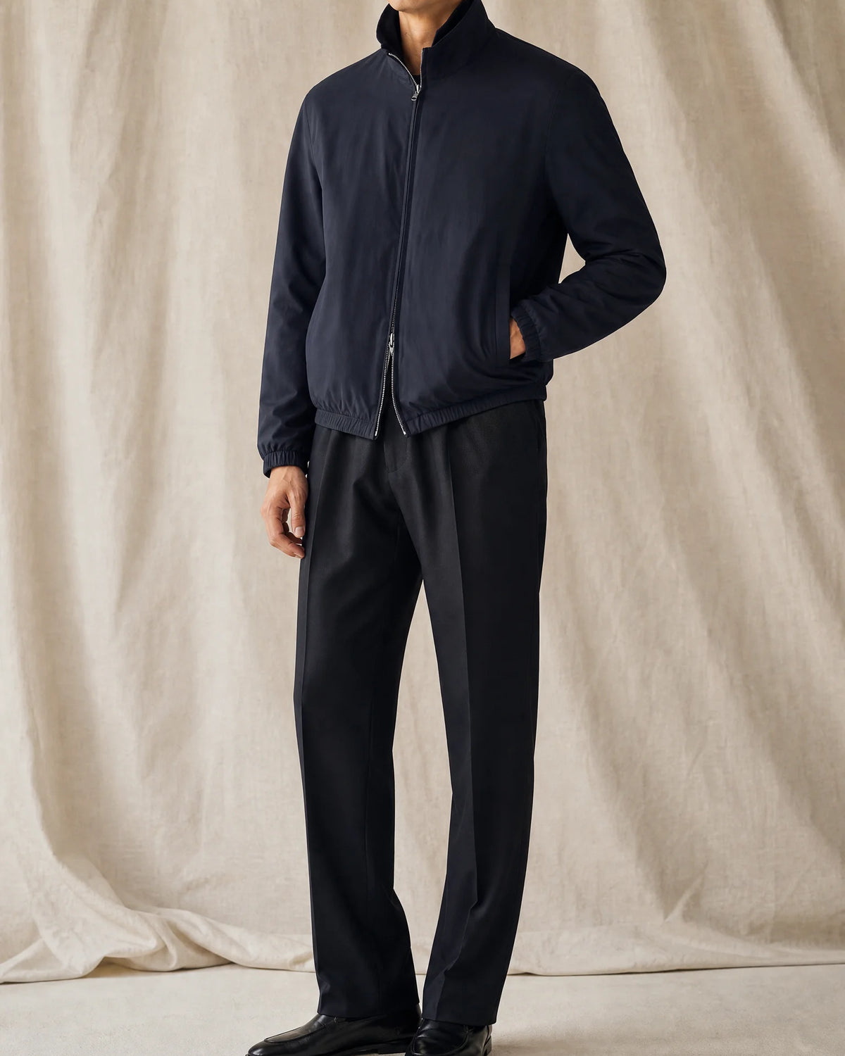 herren-studio.jpg
Mann trägt eine dunkle Blouson-Jacke mit Stoffhose und schwarzen Loafern vor neutralem Studiohintergrund.