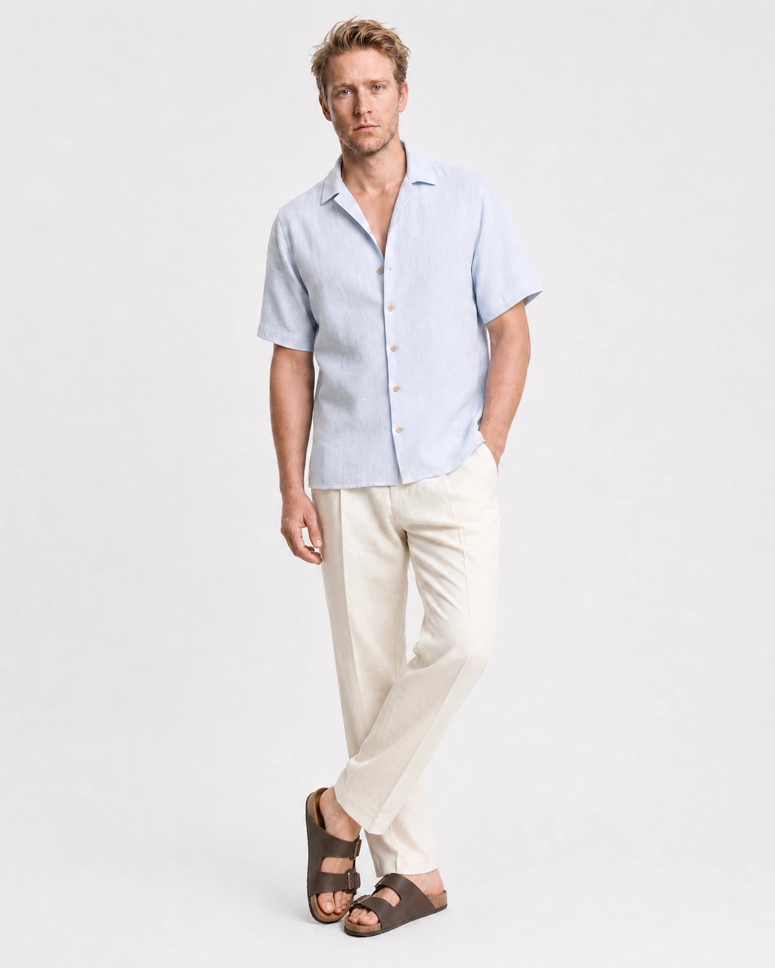 Hellblaues Leinen Kurzarmhemd Herren lässige Pose mit Händen in Taschen, cremefarbene Hose und braune Sandalen