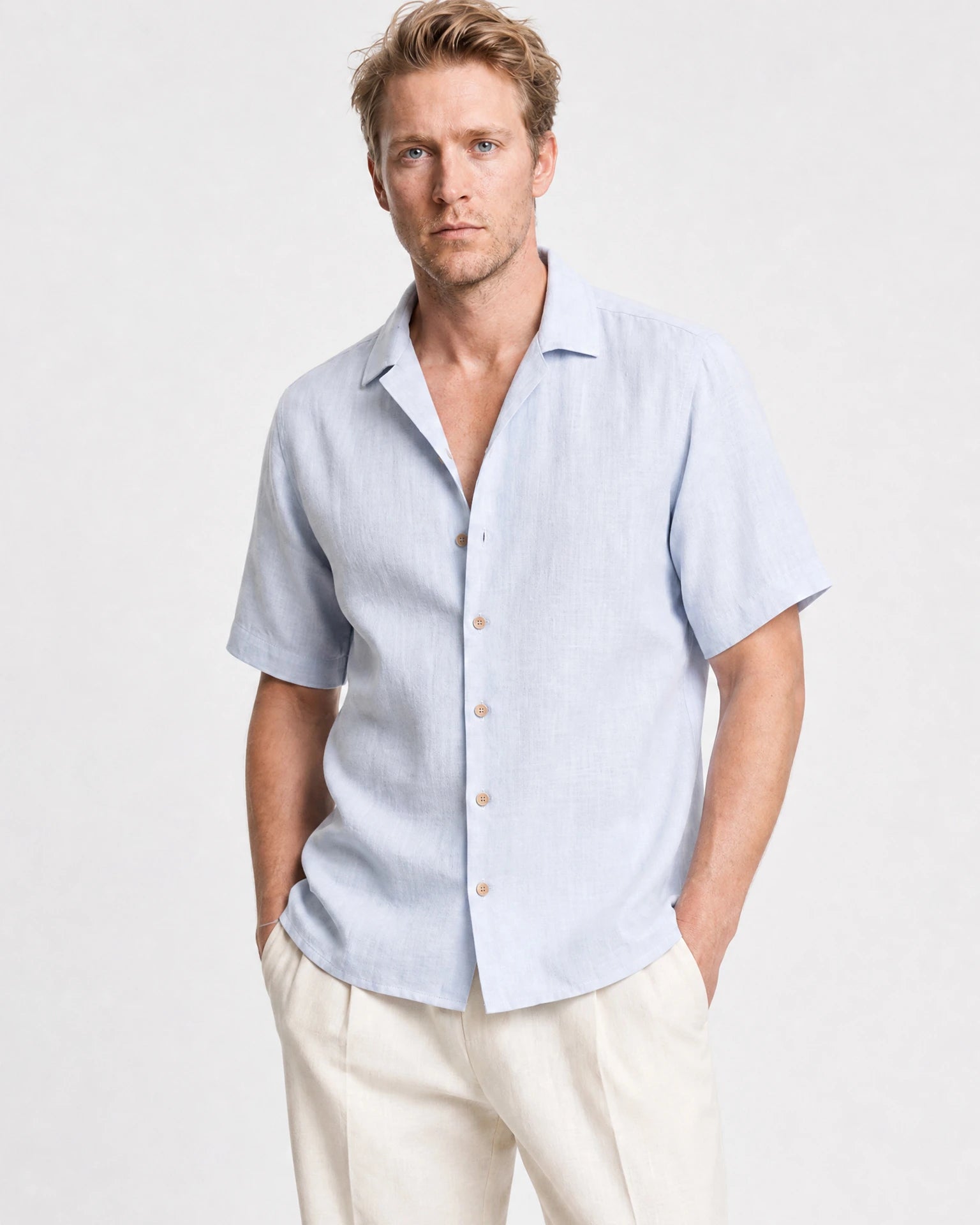 Nahaufnahme hellblaues Leinen Kurzarmhemd Herren mit Camp Collar, offener Kragen, braune Holzknöpfe, cremefarbene Hose