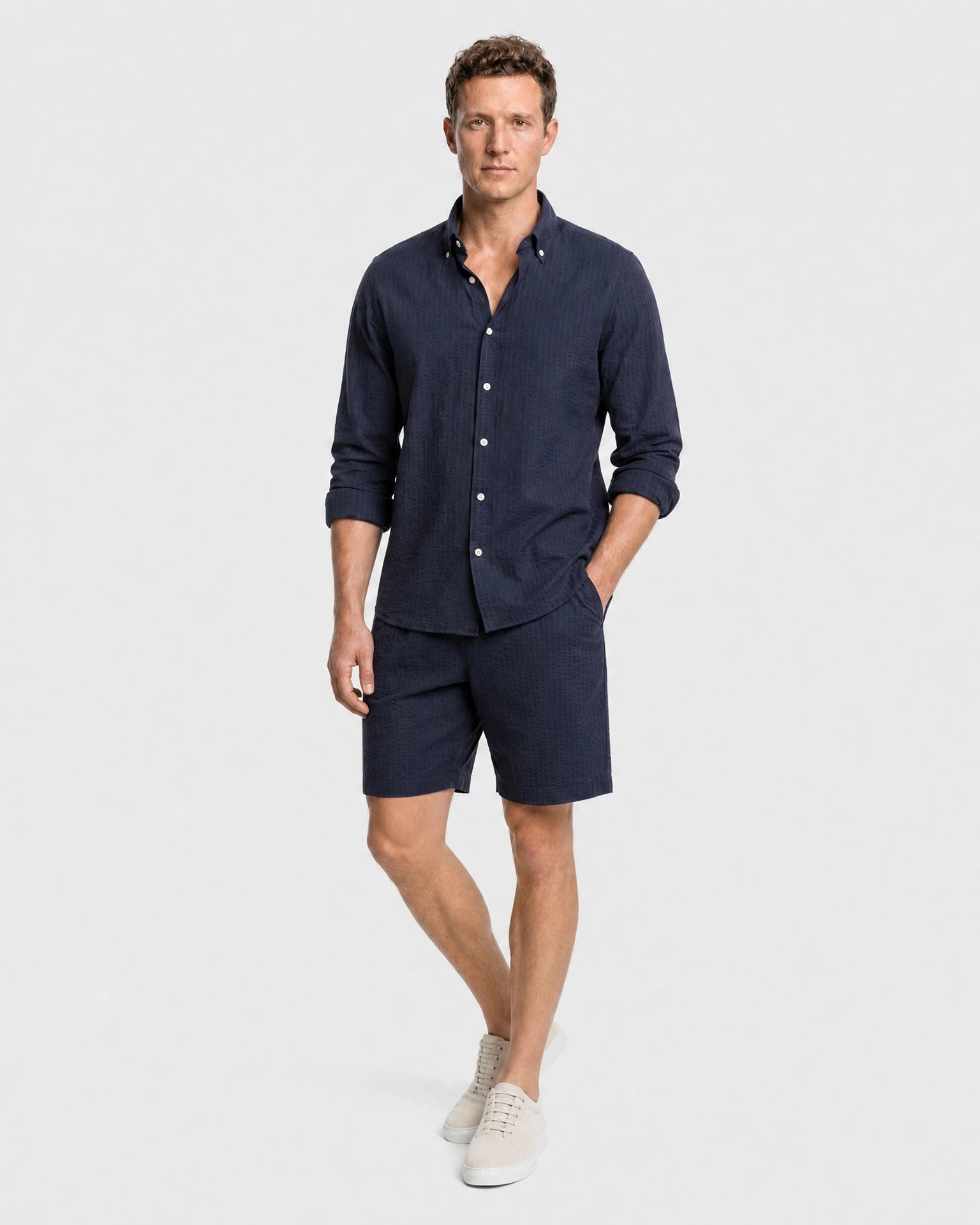 Navy Seersucker Hemd Herren Ganzkörper lässige Pose, Hand in Tasche, navy Shorts und beige Sneaker als Sommer-Outfit