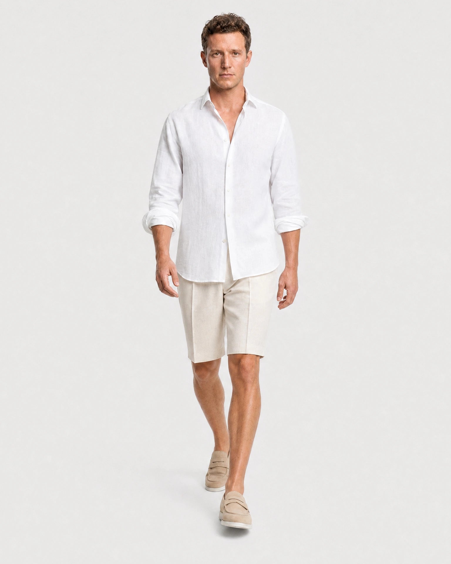 Weißes Leinen Langarmhemd Herren in Laufpose, kombiniert mit beigen Leinenshorts und beigen Suede-Loafern