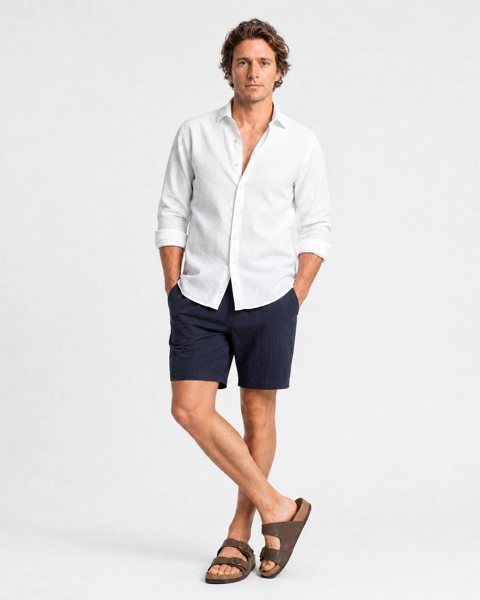 Weißes Seersucker Hemd Herren Ganzkörper lässige Pose, Hände in Taschen, navy Seersucker-Shorts und braune Sandalen