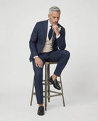 Mann im dunkelblauen Anzug mit beiger Weste auf dem Hocker sitzend