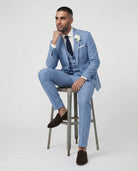 Mann im hellblauen Anzug mit Weste auf dem Hocker sitzend