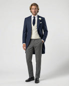 Mann im blauen Cutaway mit beiger Weste und Stresemann Hose mit Hand in der Tasche