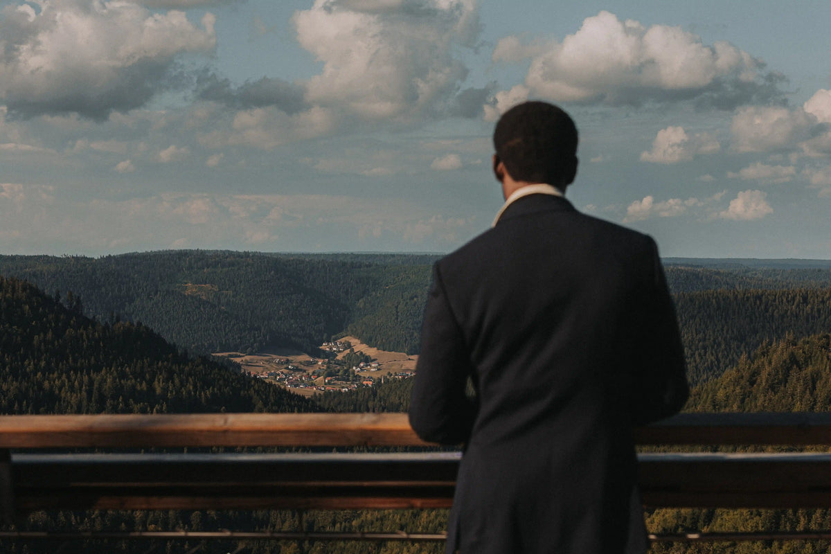 Eleganter Herrenanzug in natürlicher Kulisse: Mann blickt von einem Aussichtspunkt über Wälder, Tal und Landschaft. 