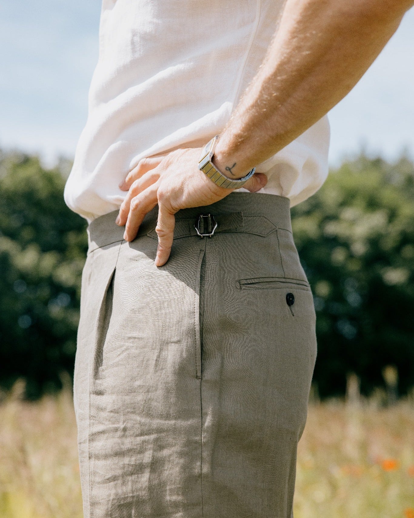 Detail einer maßgefertigten Leinenhose mit seitlicher Schnalle, Bundfalte und weißem Hemd