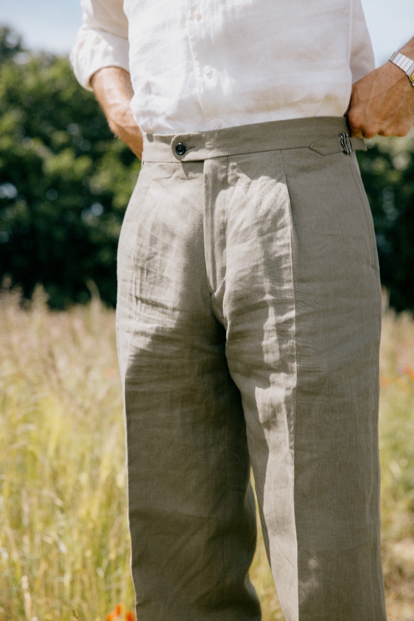Detail einer maßgefertigten Leinenhose mit seitlicher Schnalle, Bundfalte und weißem Hemd.