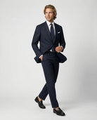 Mann im dunkelblauen Anzug aus leicht strukturierter Schurwolle mit offener Webung in Bewegung mit Hand in der Tasche
