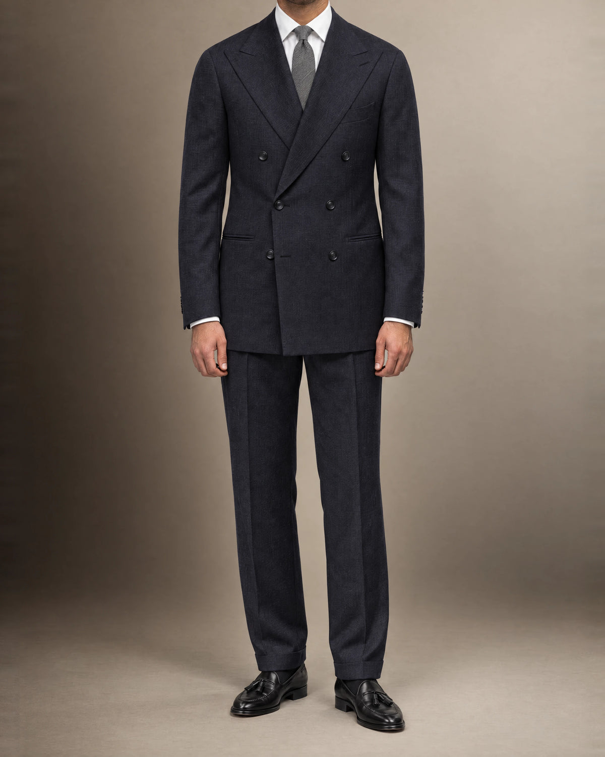 Mann im dunkelblauen Zweireiher-Anzug aus Vitale-Barberis-Canonico-Flanell mit weißem Hemd, grauer Krawatte und schwarzen Quasten-Loafern, frontal