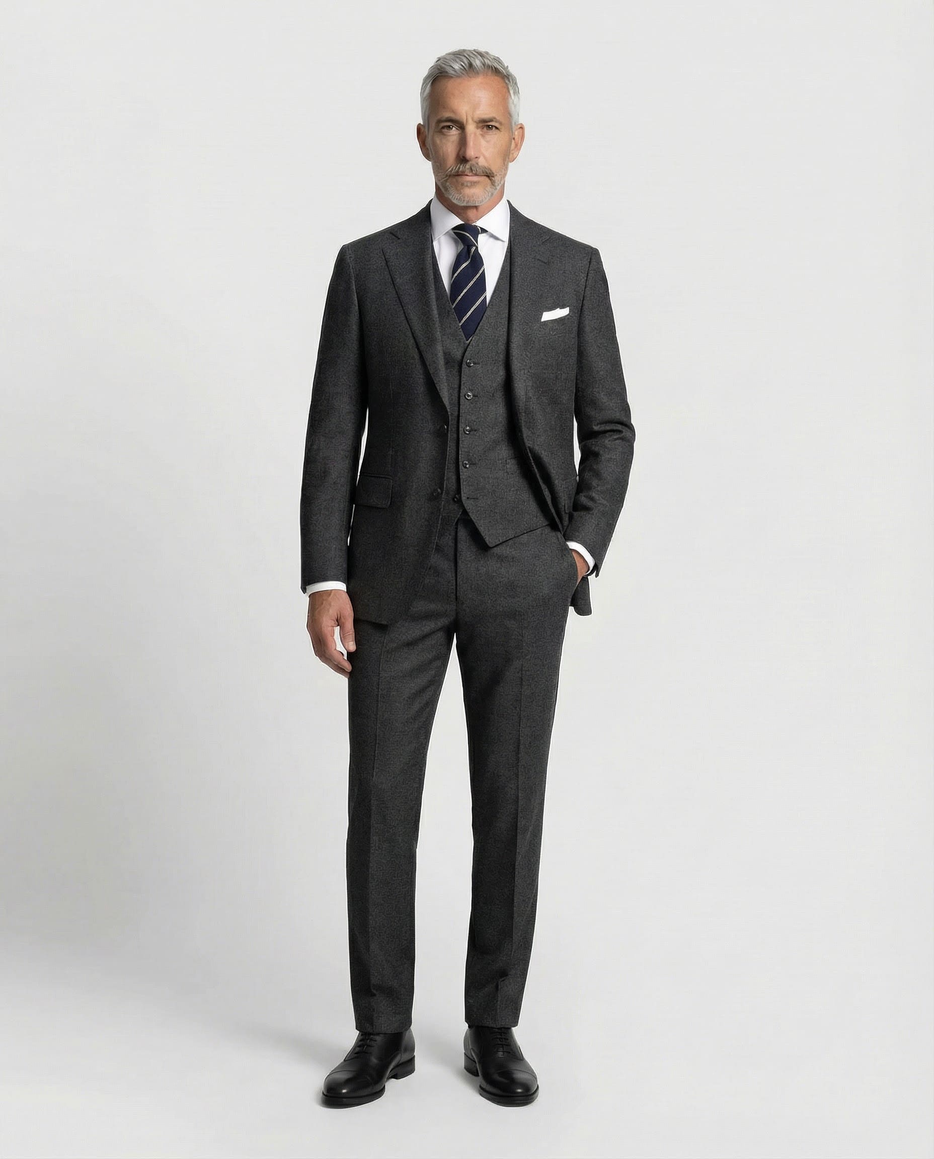 Mann im dunkelgrauen Anzug aus leicht strukturierter Schurwolle mit offener Webung mit Weste und Hand in der Tasche