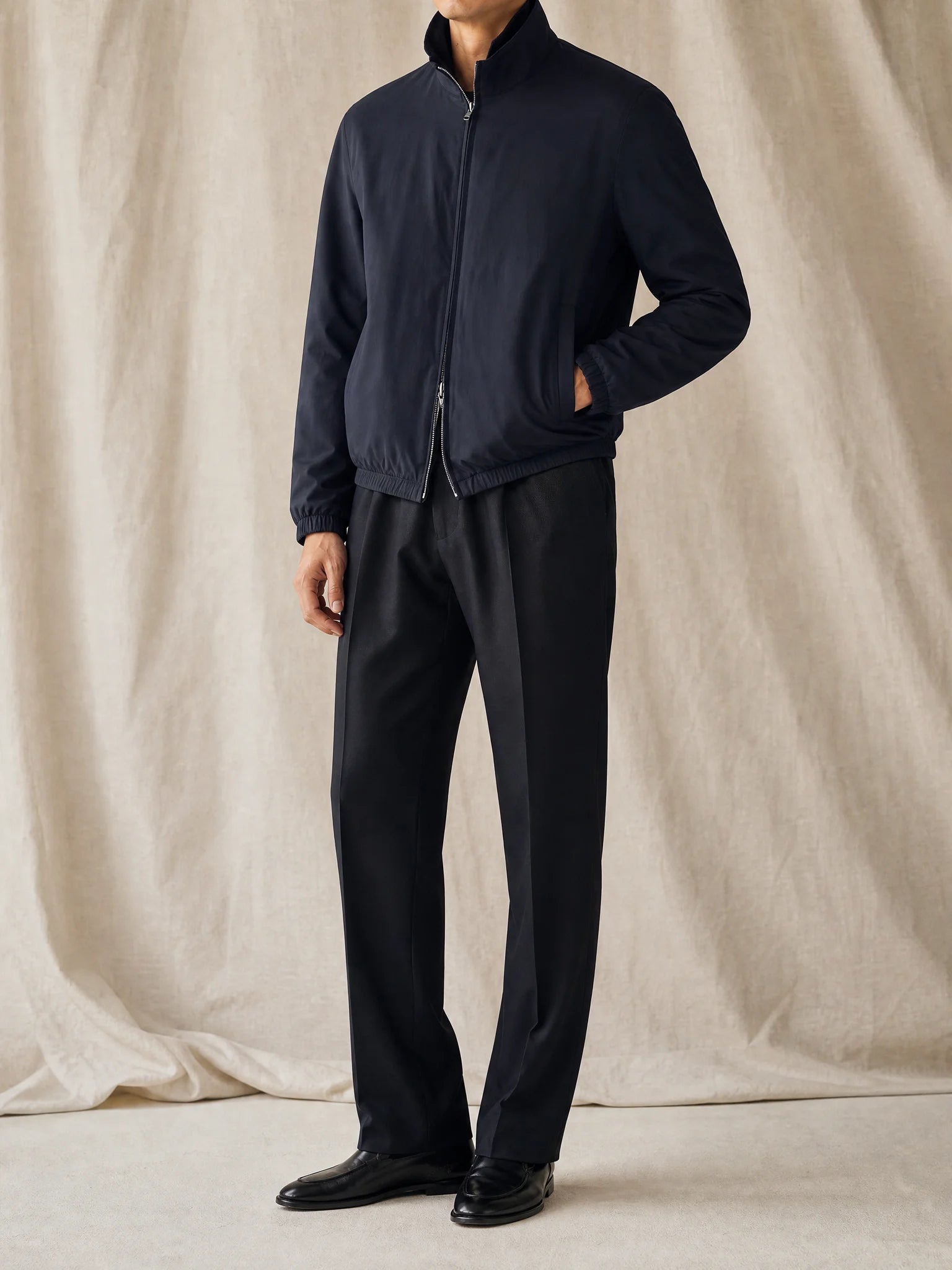 herren-studio.jpg
Mann trägt eine dunkle Blouson-Jacke mit Stoffhose und schwarzen Loafern vor neutralem Studiohintergrund.