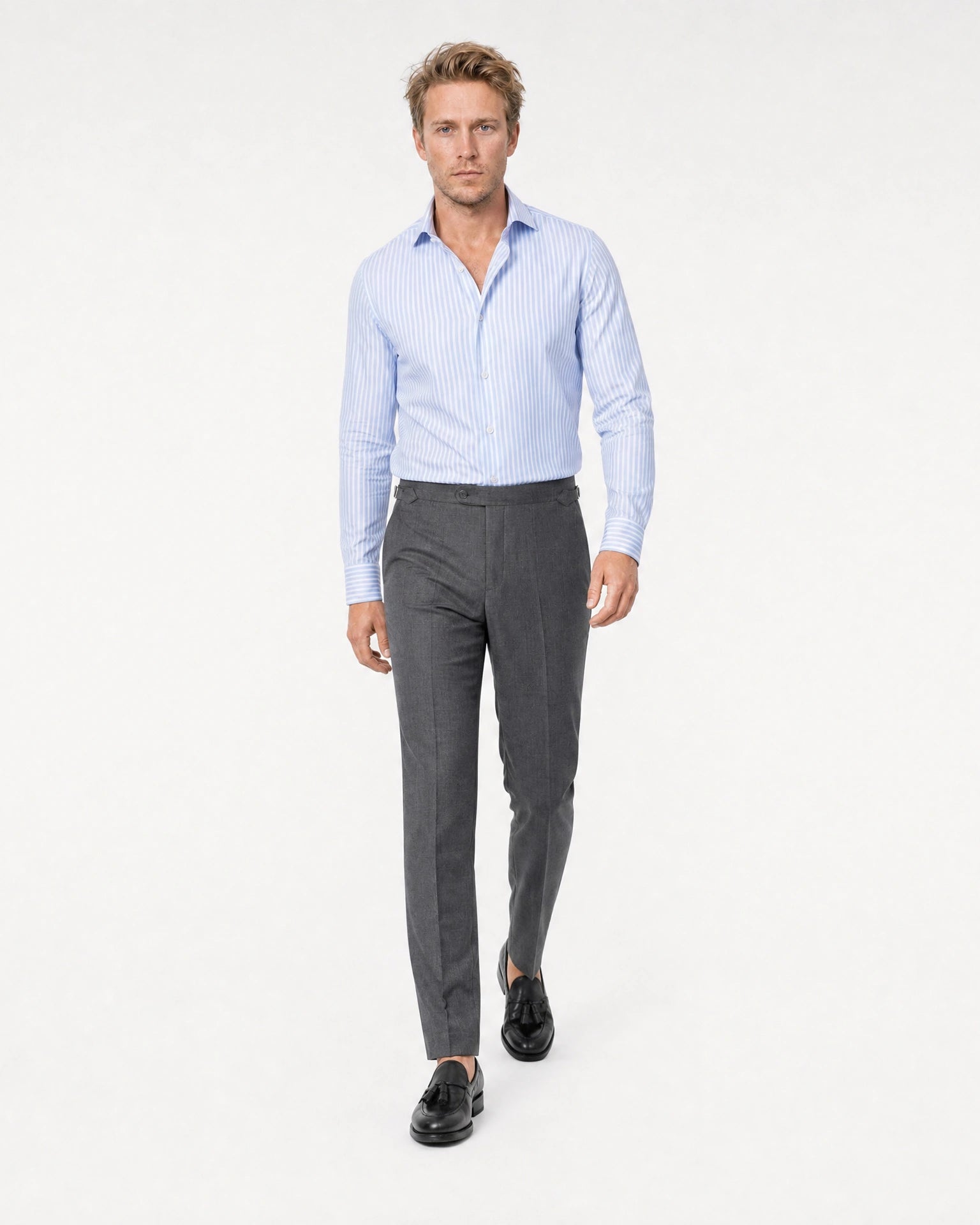 Blau-weiß gestreiftes Maßhemd Herren in Laufpose, grauer Bundfaltenhose und schwarzen Tassel-Loafern