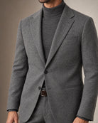 Detailansicht des grauen Flanellanzugs mit Zweiknopf-Sakko, Paspeltaschen, grauem Rollkragenpullover und braunem Wildledergürtel