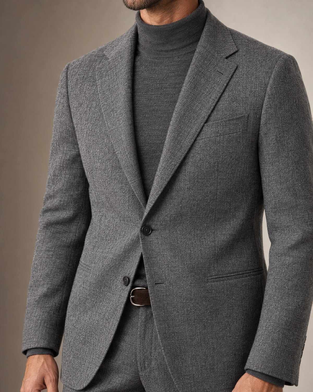 Detailansicht des grauen Flanellanzugs mit Zweiknopf-Sakko, Paspeltaschen, grauem Rollkragenpullover und braunem Wildledergürtel