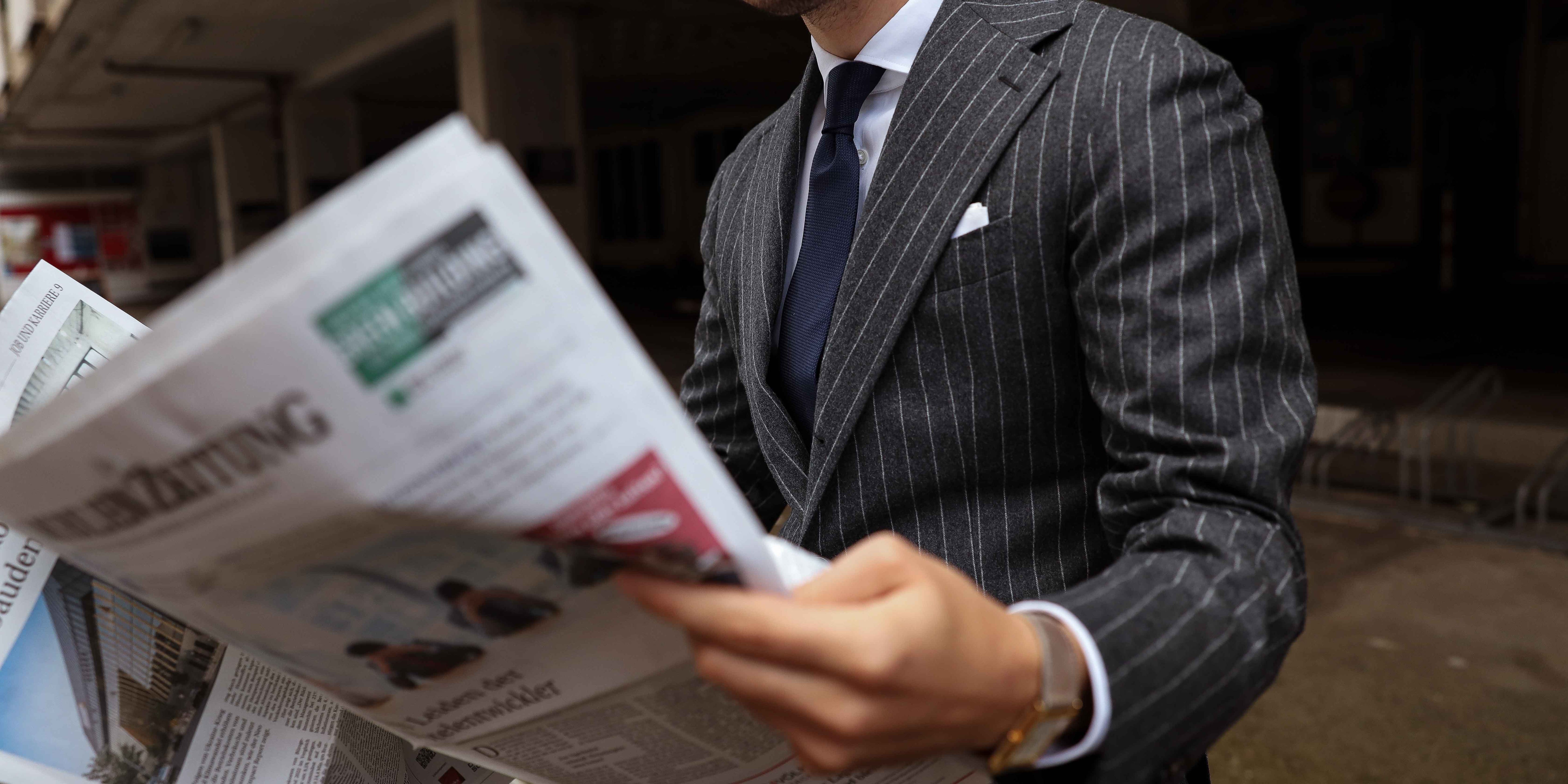 Kunde im dnunkelgrauen Anzug mit Kreidestreifen liest eine Zeitung