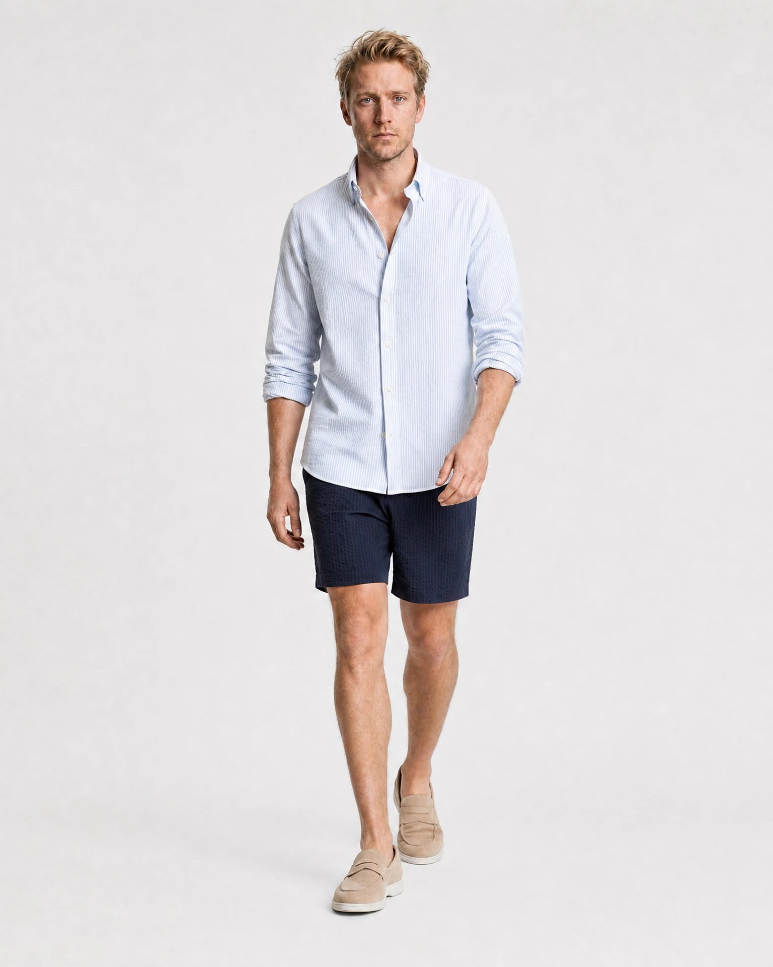 Hellblau-weiß gestreiftes Seersucker Hemd Herren in Laufpose, navy Seersucker-Shorts und beige Suede-Loafer