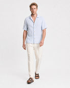 Hellblaues Leinen Kurzarmhemd Herren in Laufpose, cremefarbene Leinenhose und braune Sandalen, sommerlicher Look
