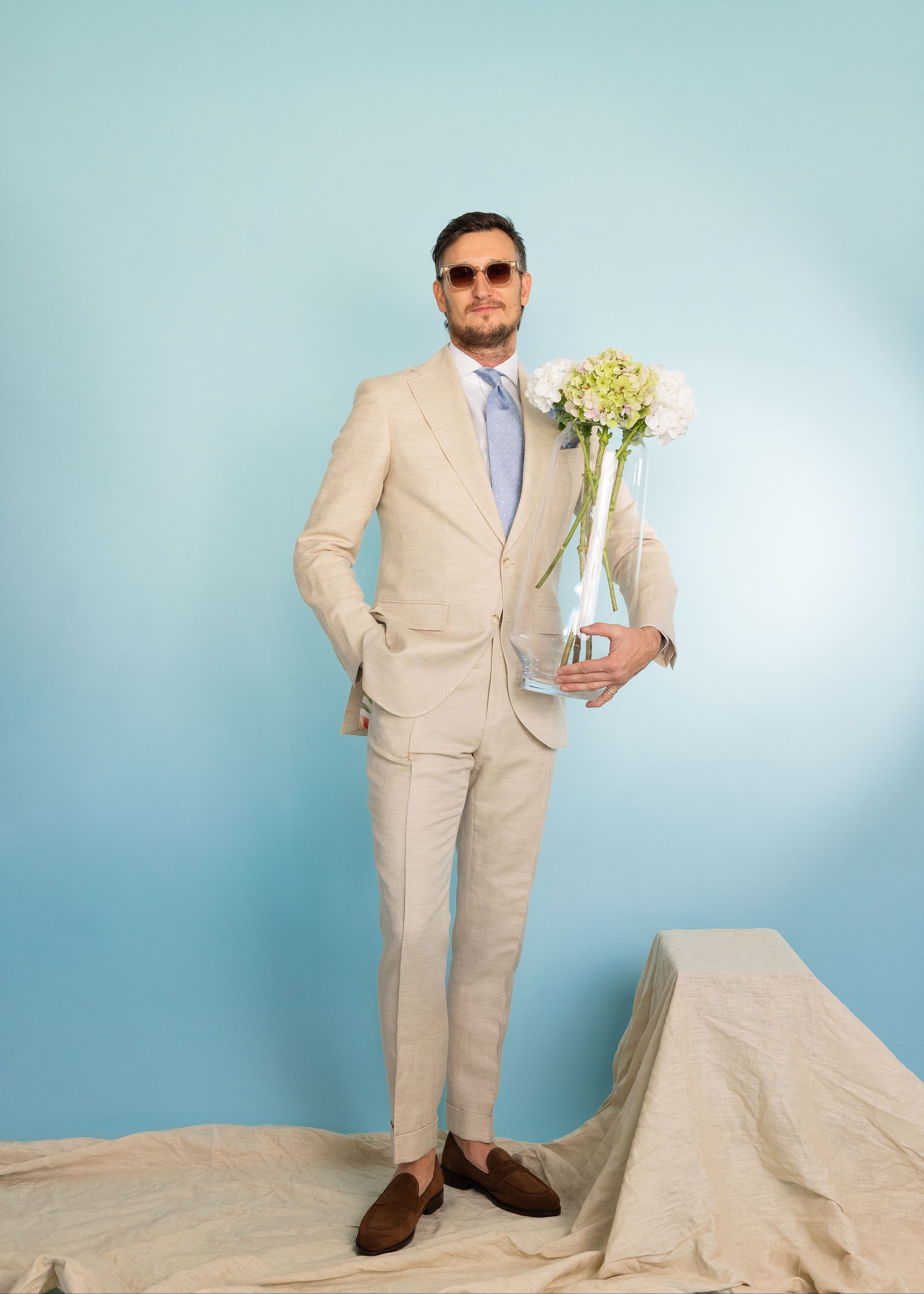 Viktor steht vor hellblauer Wand mit einem Blumenstrauß samt Vase in der Hand