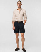 Sand-beiges Leinen Herringbone Hemd Herren Ganzkörper frontal, navy Bundfaltenshorts, brauner Flechtgürtel und braune Suede-Loafer