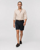Sand-beiges Leinen Herringbone Hemd Herren in Laufpose, navy Bundfaltenshorts mit braunem Flechtgürtel und braunen Suede-Loafern