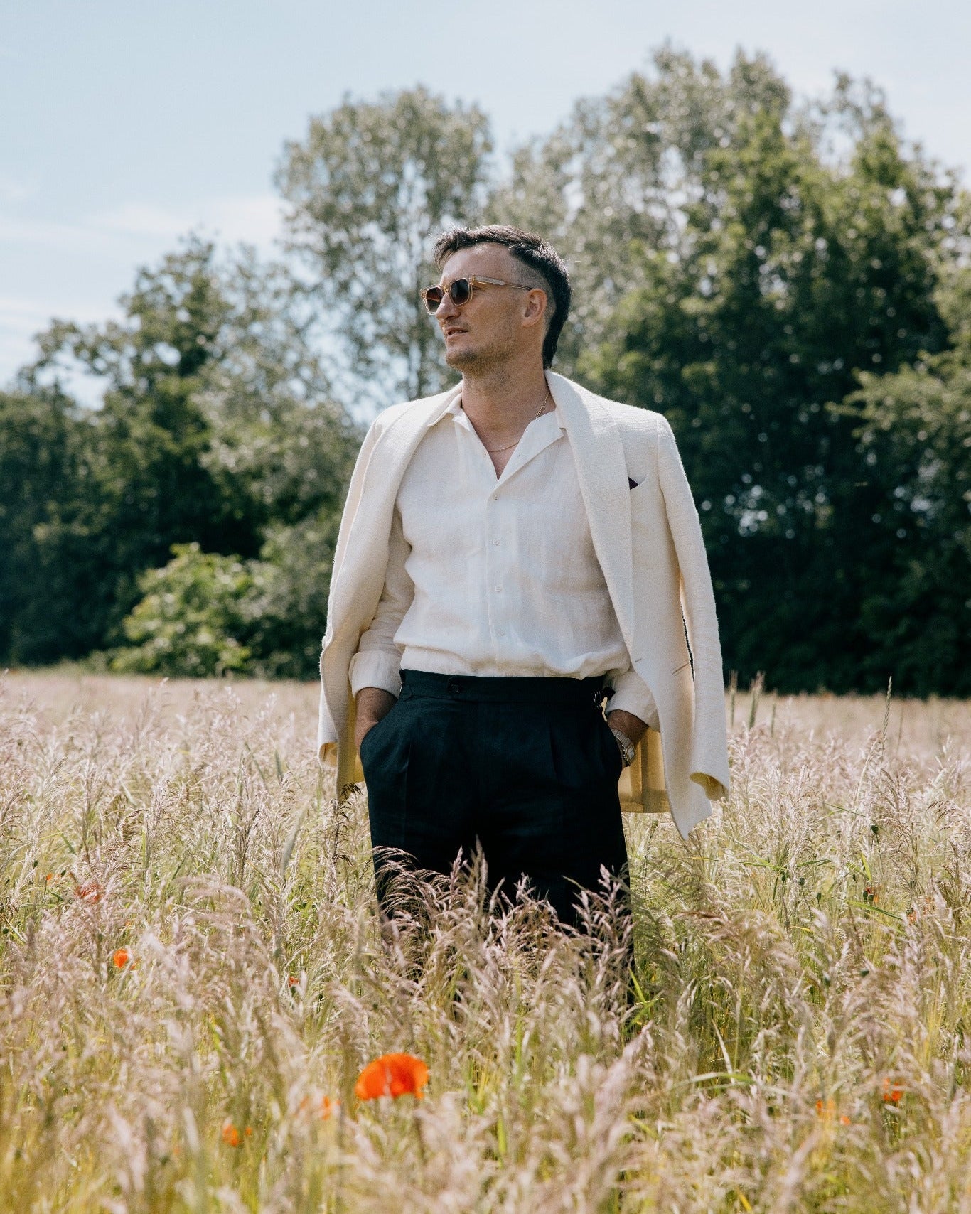 Eleganter Sommerlook mit weißem Sakko, Leinenhemd und schwarzer Leinenhose auf einer Wiese