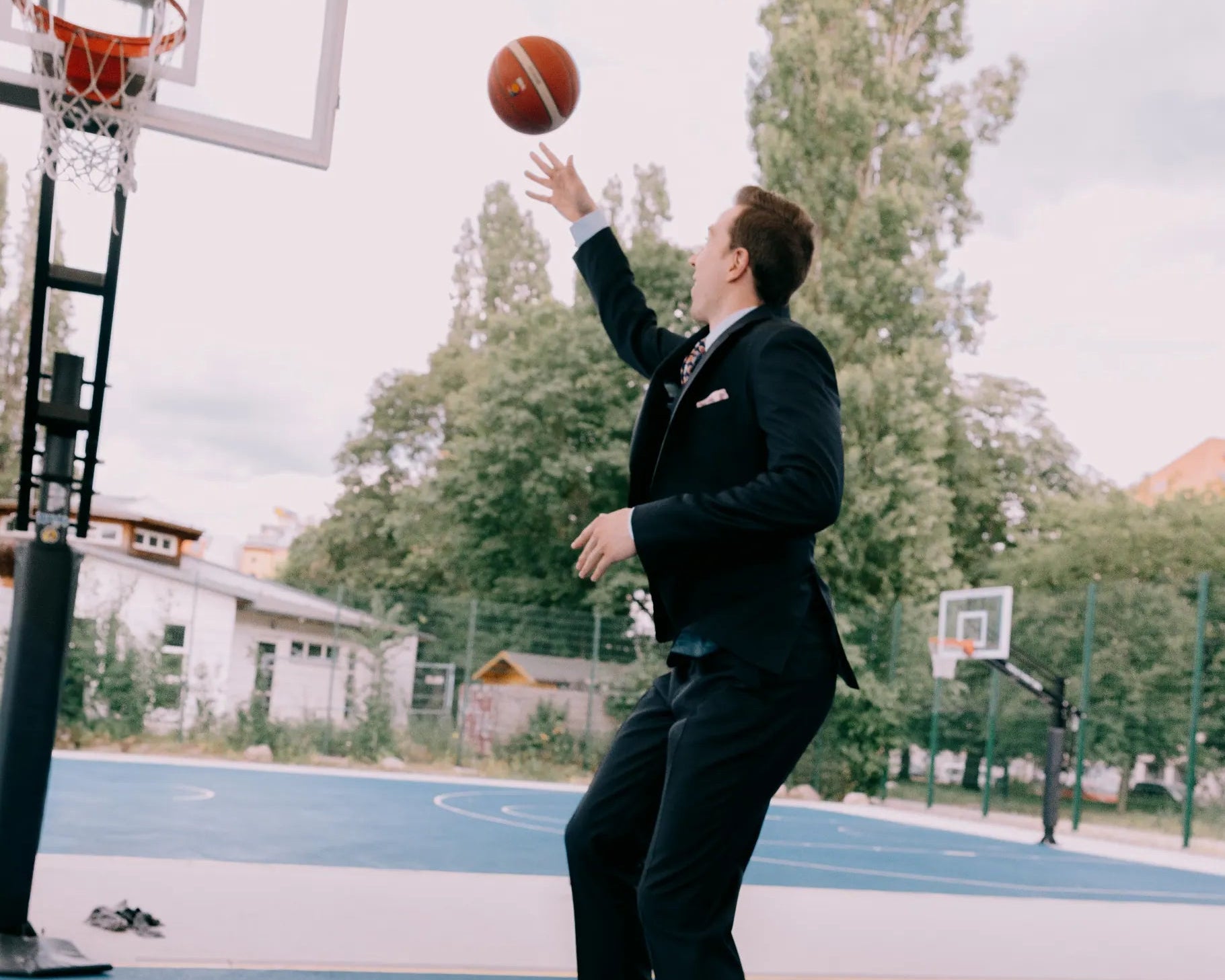 Mann im dunklen Maßanzug wirft einen Basketball auf einem urbanen Court und kombiniert klassischen Business-Stil mit sportlicher Bewegung