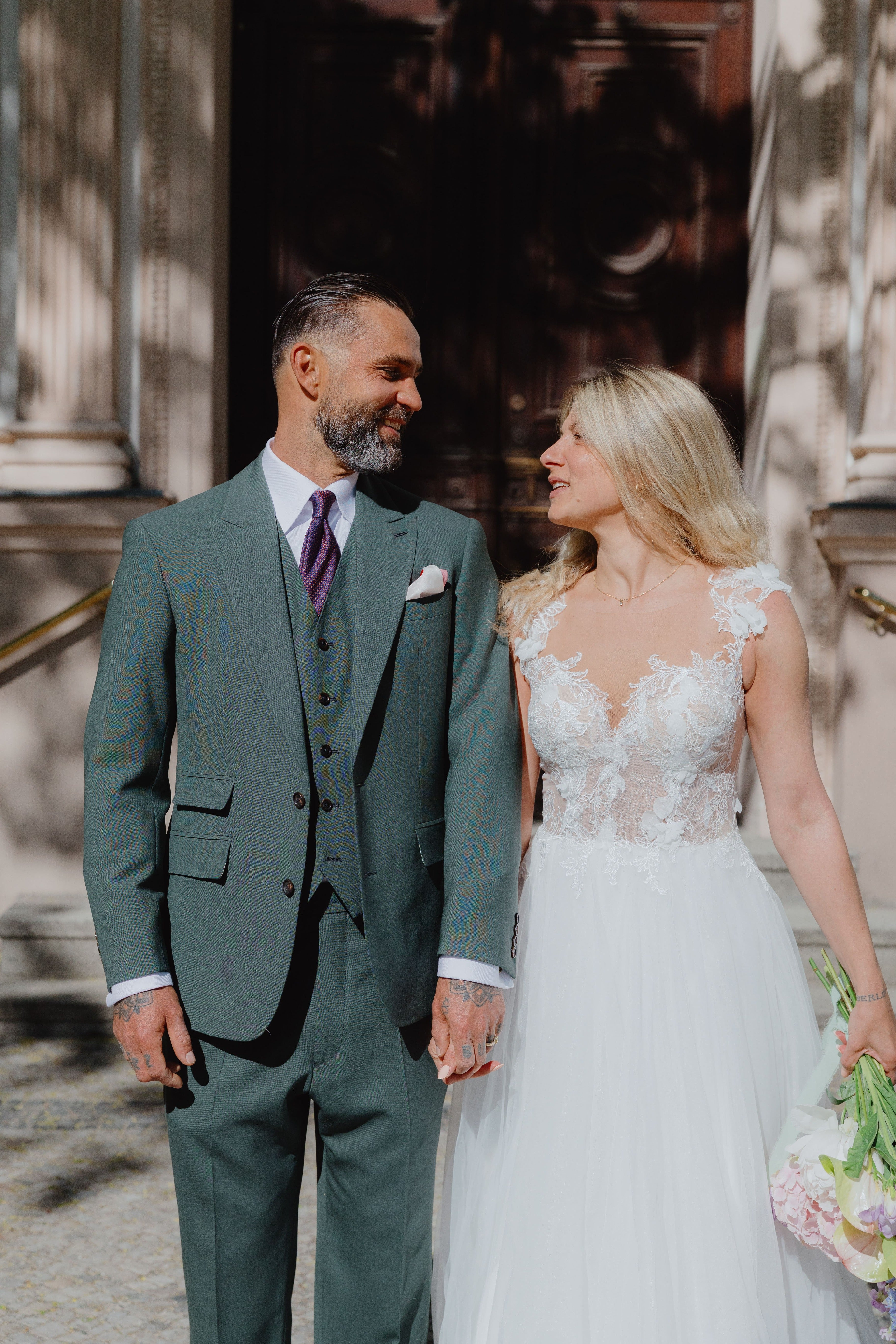 Hochzeitspaar steht vor einer alten Tur, Die Frau im Hochzeitskleid und der Mann im grünen Dreiteiler.