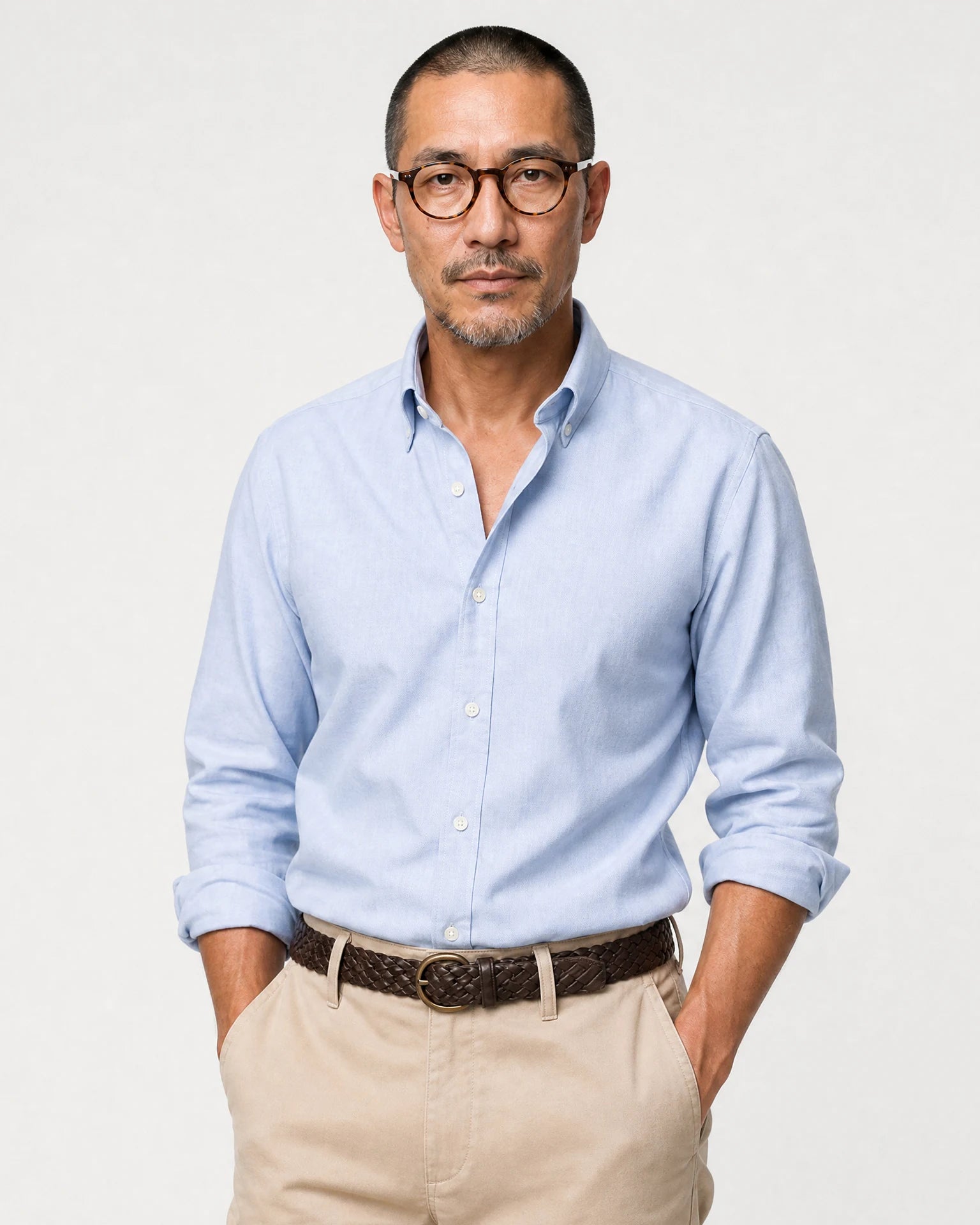 Halbkörperansicht eines Models mit hellblauem Oxford-Hemd, beiger Hose und braunem Gürtel.