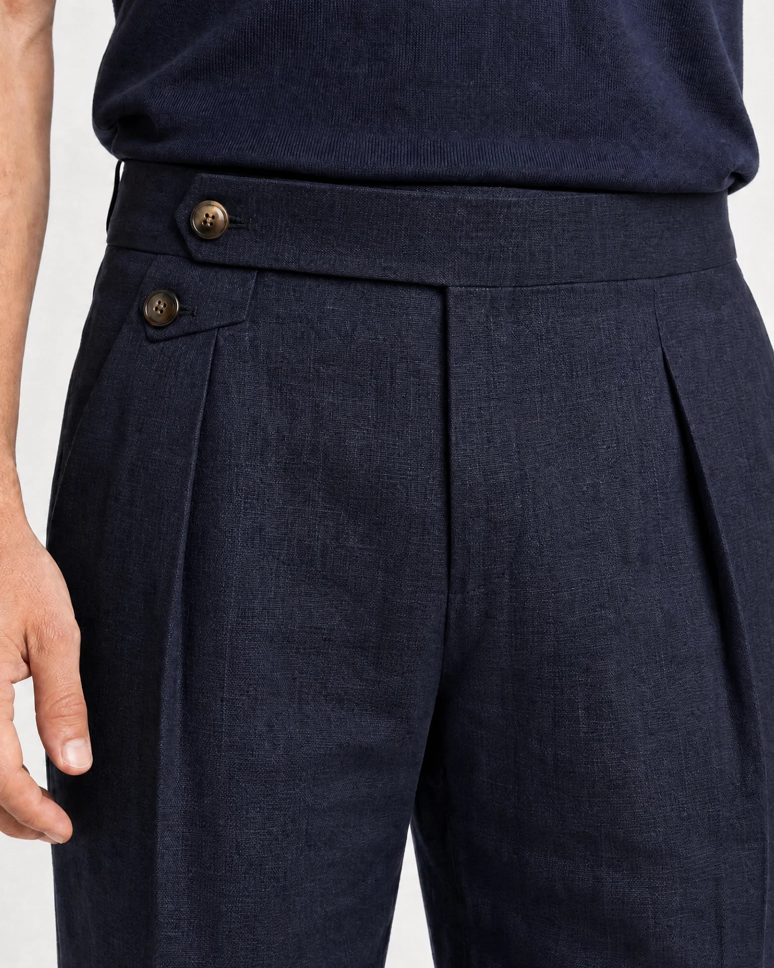 Detailaufnahme der navyblauen Leinenhose mit Bundfalte, seitlichem Versteller mit Knöpfen und dunkelblauem Strickshirt.
