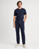 Ganzkörperansicht eines Models in navyblauer Leinenhose mit dunkelblauem T-Shirt und hellen Sneakern.