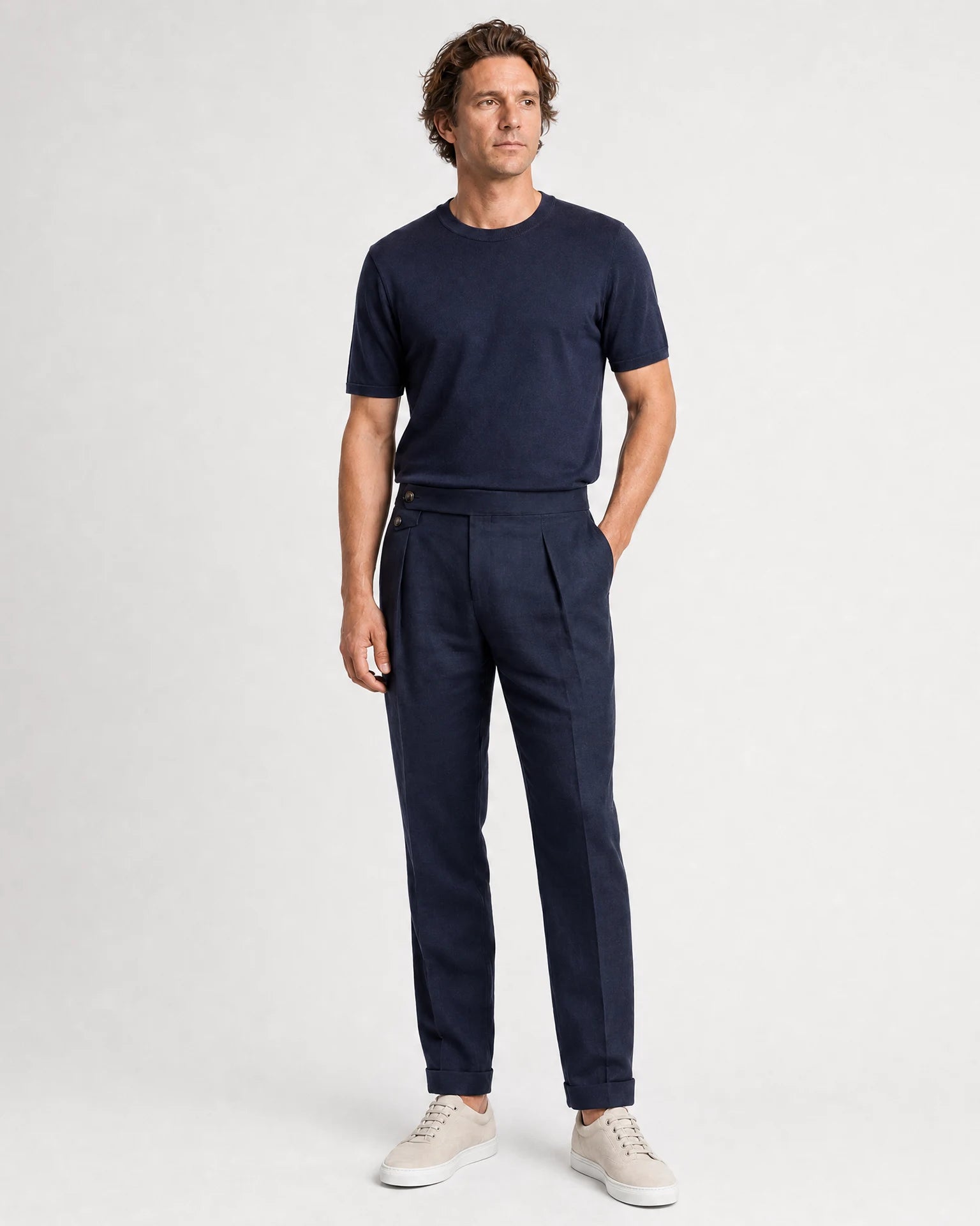 Ganzkörperansicht eines Models in navyblauer Leinenhose mit dunkelblauem T-Shirt und hellen Sneakern.