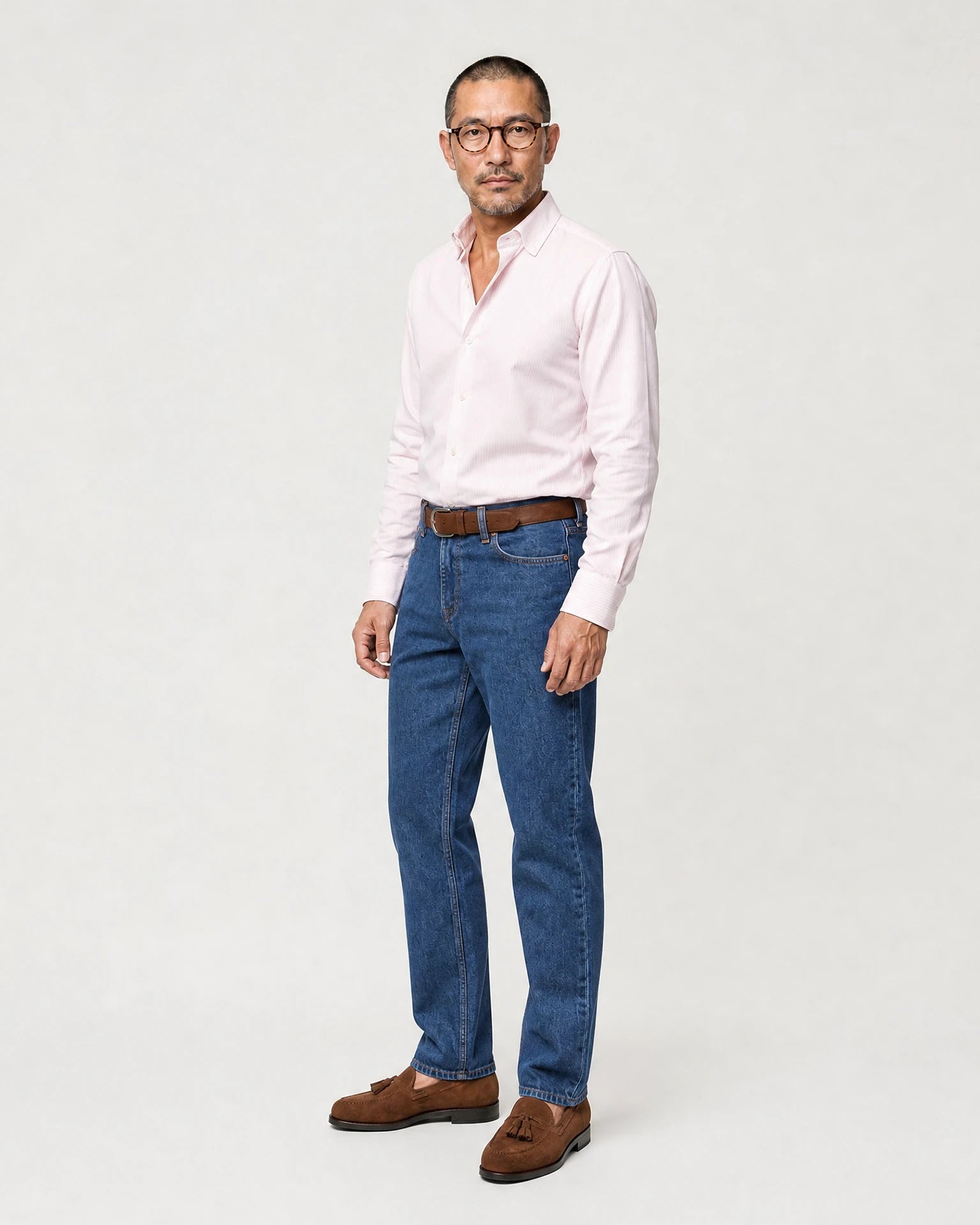 Seitenansicht eines Models mit rosa-weiß gestreiftem Oxford-Hemd, Jeans und braunen Loafern.
