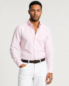 Ganzkörperansicht eines Models mit roséfarbenem Oxford-Hemd, weißer Hose und braunen Loafern.