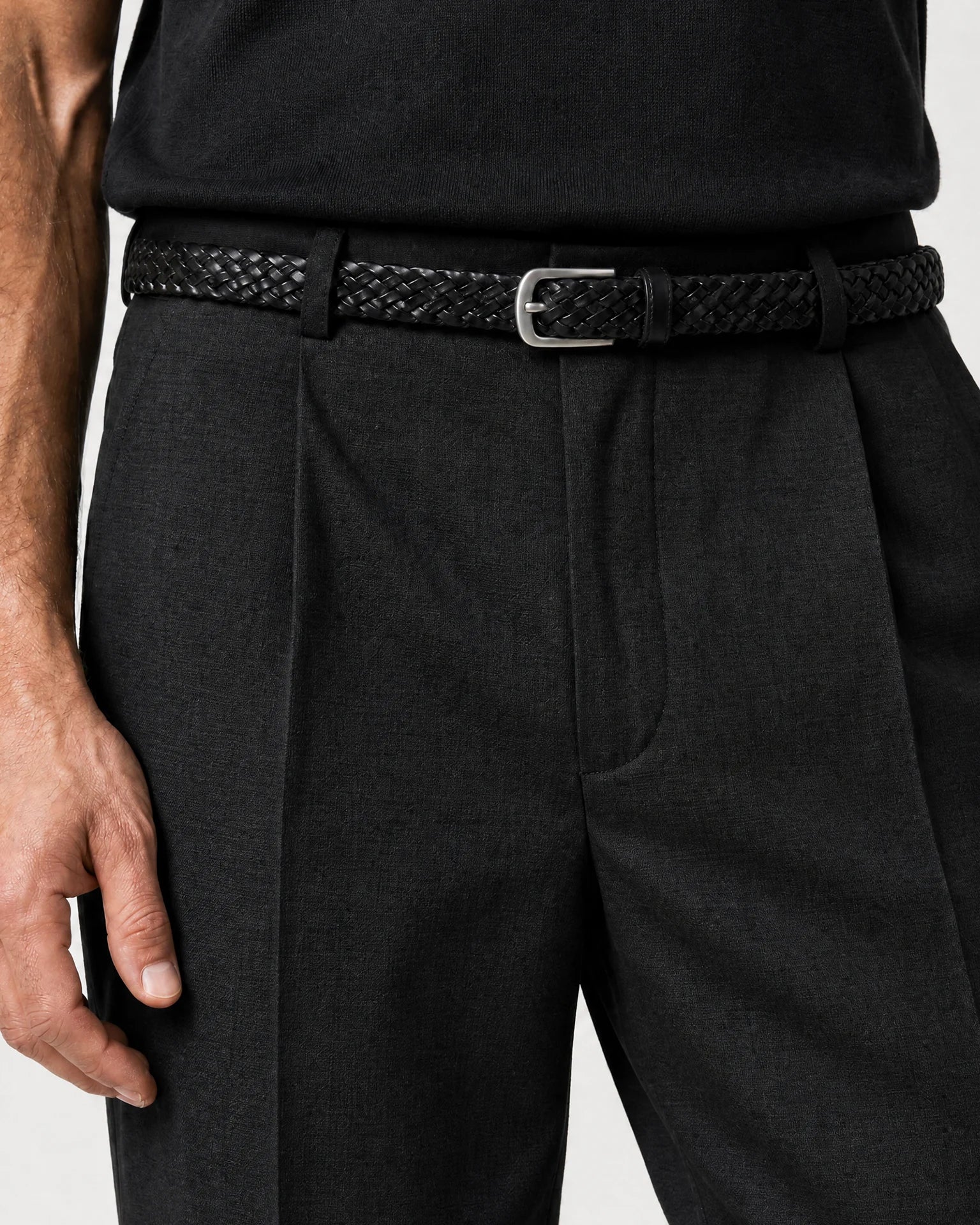 Detailaufnahme der schwarzen Leinenhose mit Bundfalten, schwarzem geflochtenem Gürtel und strukturierter Leinenoberfläche.
