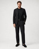 Schwarze Leinenhose kombiniert mit schwarzem Sakko, schwarzem Shirt, schwarzem Gürtel und schwarzen Loafern in einer Ganzkörperansicht.