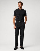 Ganzkörperansicht eines Models in schwarzer Leinenhose mit schwarzem T-Shirt, schwarzem Gürtel und schwarzen Loafern.