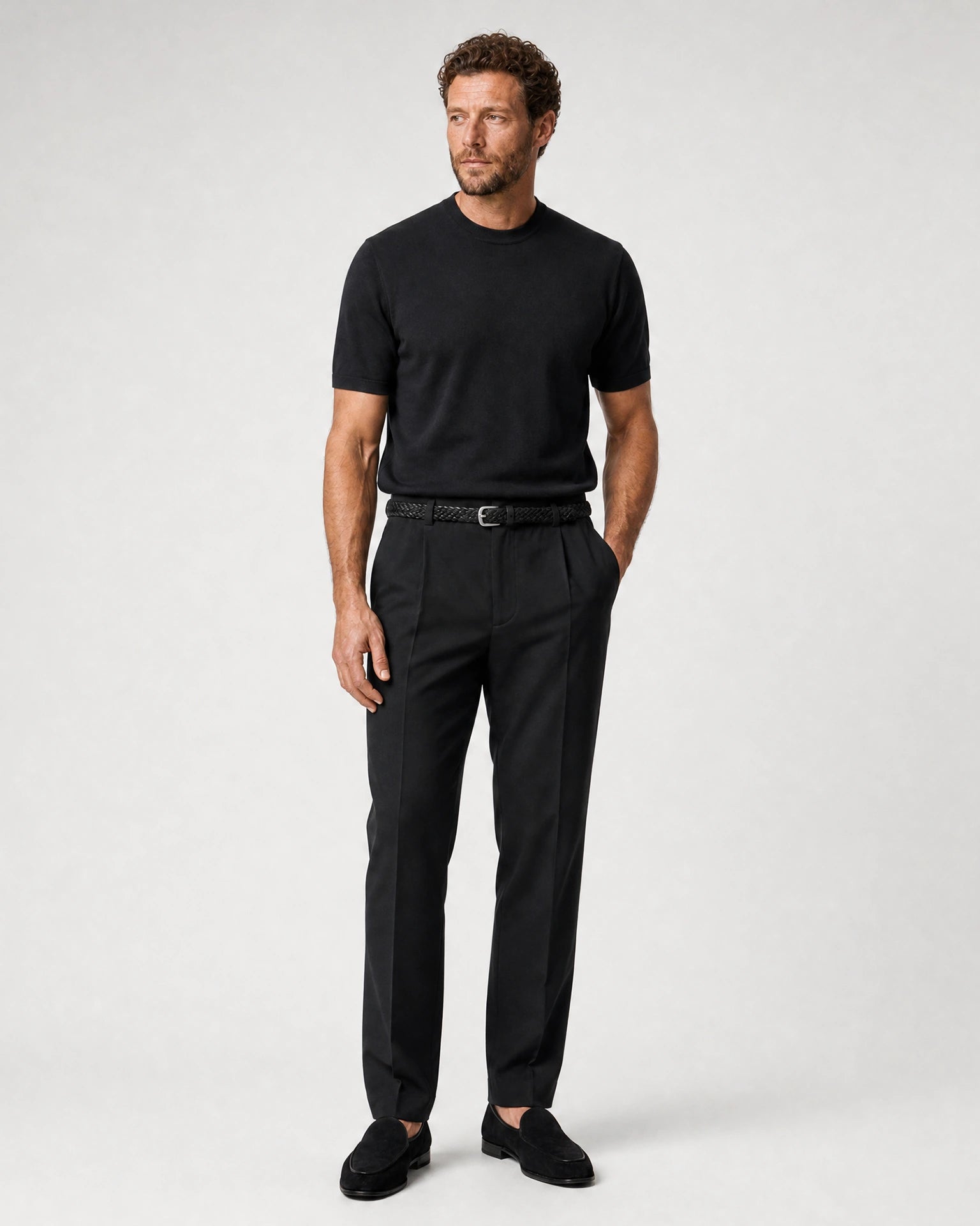 Ganzkörperansicht eines Models in schwarzer Leinenhose mit schwarzem T-Shirt, schwarzem Gürtel und schwarzen Loafern.