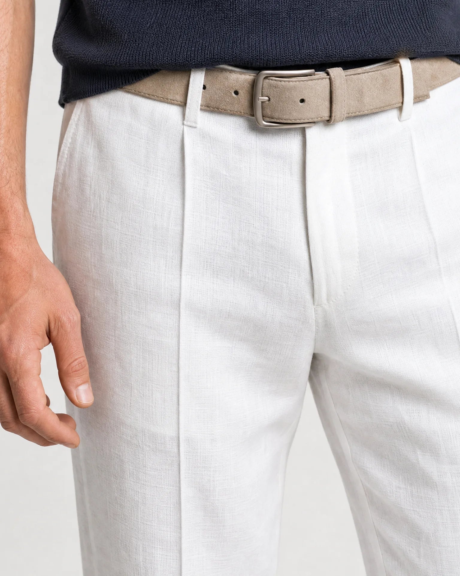Detailaufnahme der weißen Leinenhose mit Bundfalte, beigem Gürtel und strukturierter Leinenoberfläche.