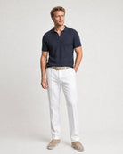 Weiße Leinenhose kombiniert mit navy Poloshirt, beigem Gürtel und hellen Loafern in einer Ganzkörperansicht.