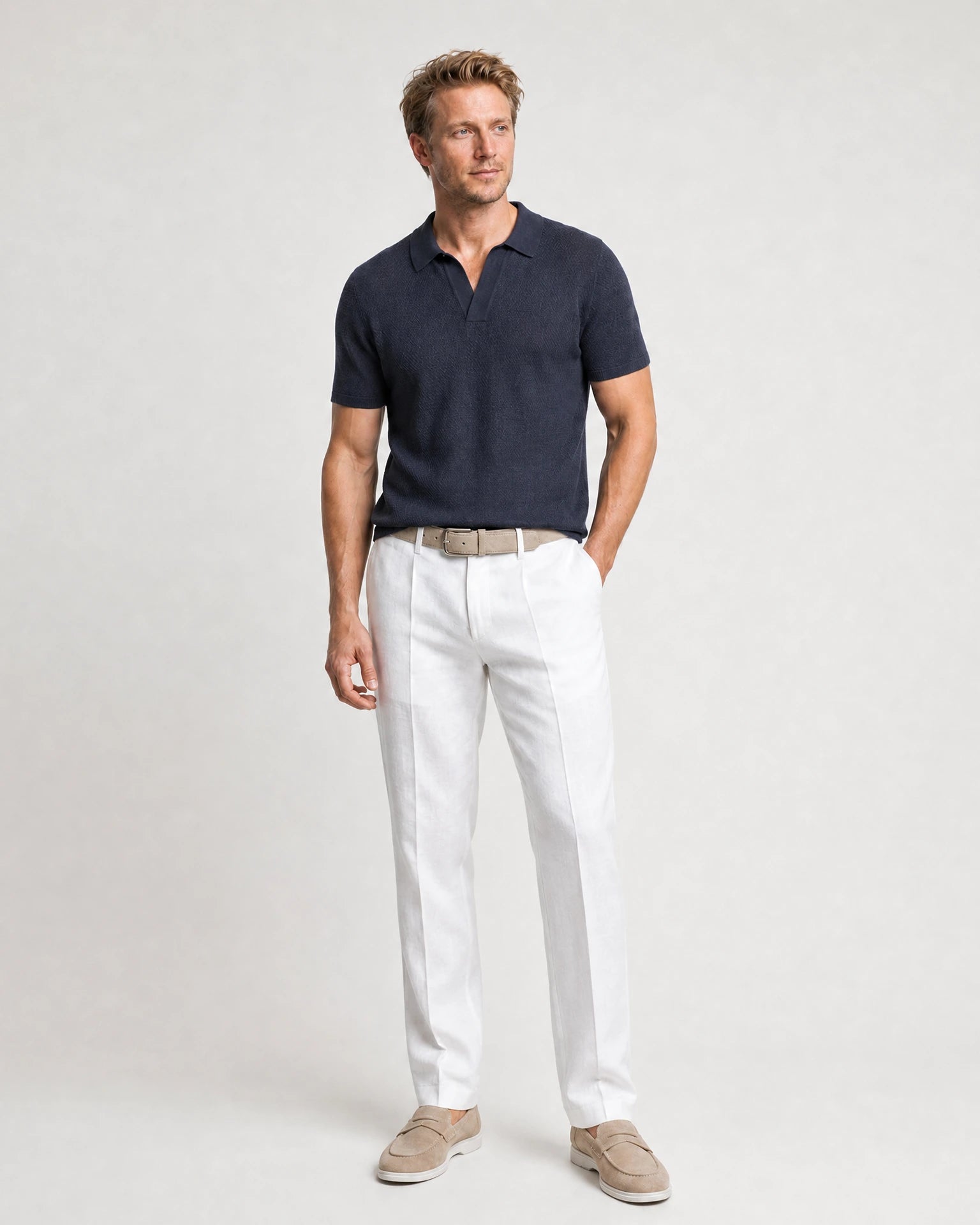 Weiße Leinenhose kombiniert mit navy Poloshirt, beigem Gürtel und hellen Loafern in einer Ganzkörperansicht.