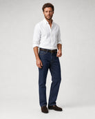 Herren Oxford-Hemd in Weiß kombiniert mit dunkler Jeans, braunem Gürtel und braunen Loafern.