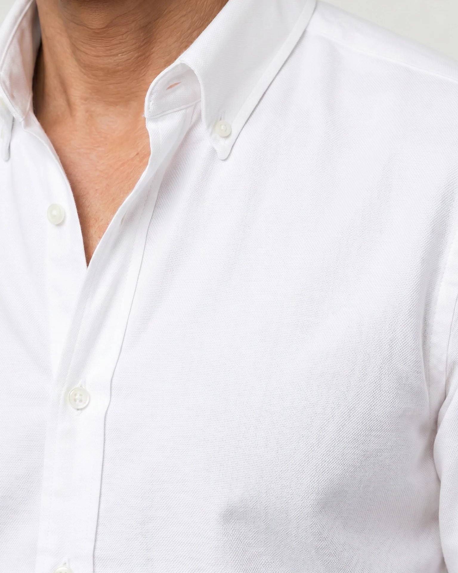 Detailaufnahme des weißen Oxford-Hemds mit Button-Down-Kragen, strukturierter Webung und weißen Knöpfen.
