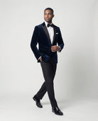 Mann im dunkelblauen Samtsakko mit schwarzer Hose in Bewegung mit Hand in der Tasche seitlich abgebildet