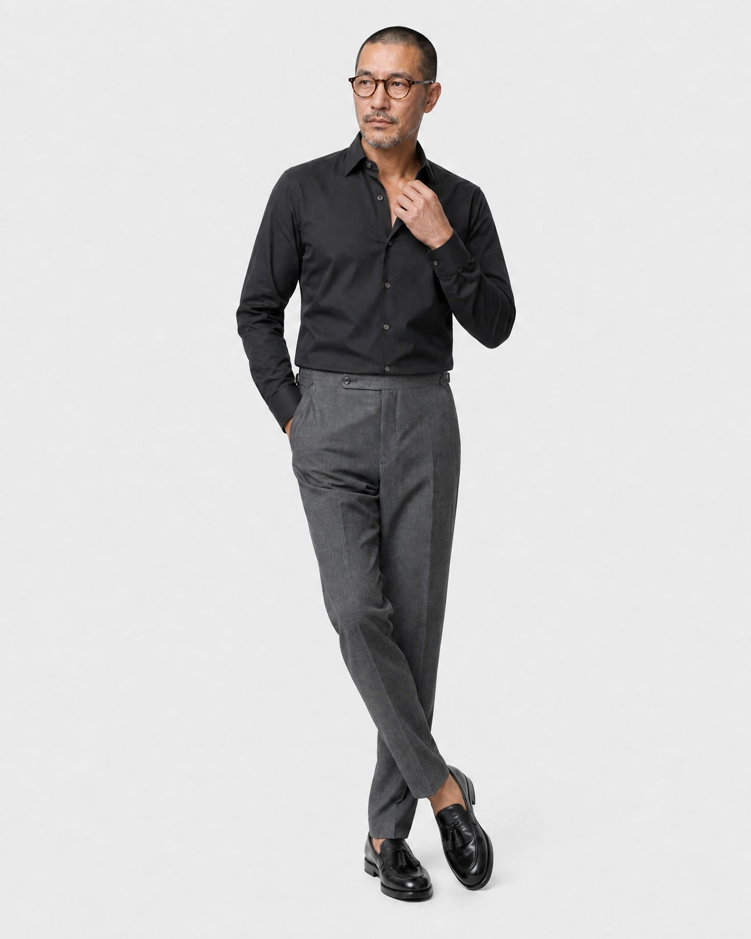 Schwarzes Maßhemd Herren in lässiger Pose, Kragen greifend, grauer Bundfaltenhose und Tassel-Loafern
