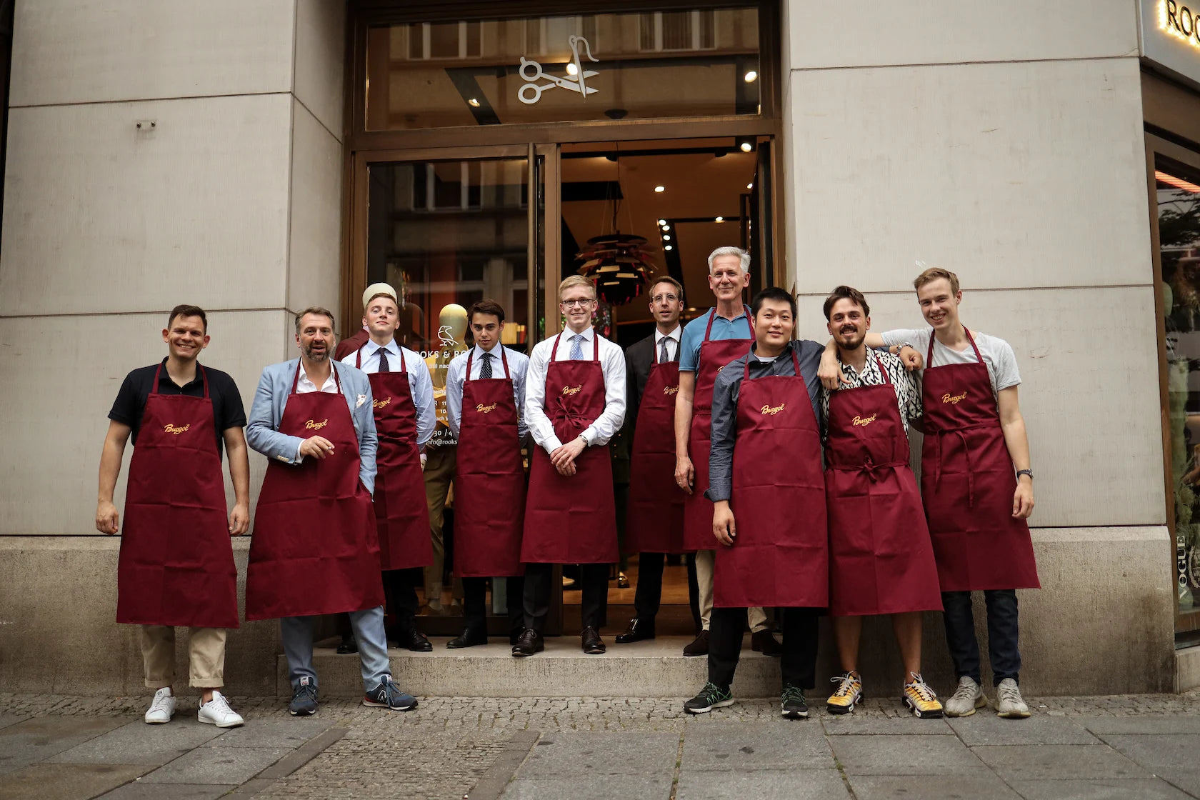 Gruppe von Männern mit roten Schürzen steht vor dem ROOKS & ROCKS Store bei einem gemeinsamen Team- oder Kundenevent