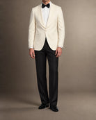 Mann im cremeweißen Dinnerjacket mit Schalkragen, schwarzer Smokinghose, Fliege und Lack-Loafern in frontaler Ganzkörperansicht
weisses-dinnerjacket-schalkragen-detail-fliege.webp	