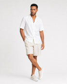 Weißes Leinen Kurzarmhemd Herren Ganzkörper mit seitlichem Blick, beige Leinenshorts, Sneaker, entspannte Sommerposes
